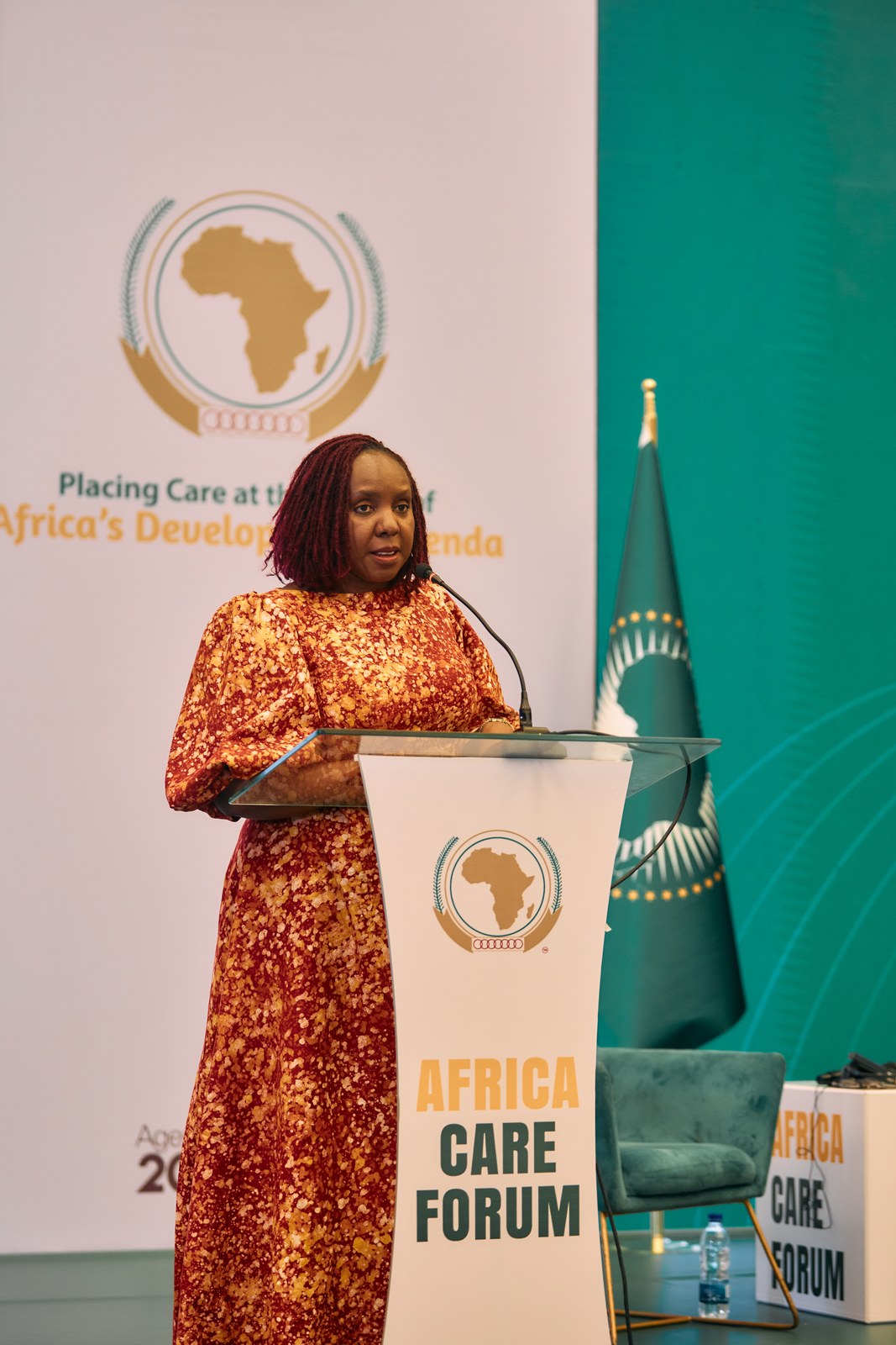 Speaker at the podium beside the African Union flag at the Africa Care Forum
